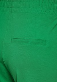 Shorts en coton verts avec une taille élastique et une poche arrière décorative avec une ouverture étroite. Texture lisse et couleur unie.