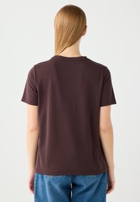 Krótki rękaw, brązowy t-shirt wykonany z miękkiego materiału. Posiada okrągły dekolt i luźny krój, zestawiony z jasnoniebieskimi spodniami w wysokim stanie.