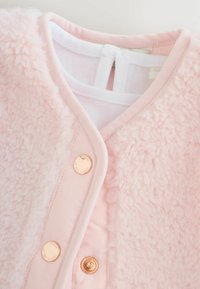 Bāls rozā vilnas jaka ar mīkstu tekstūru, ar gludu priekšējo paneļa daļu, rozīgu zelta pogām un baltu iekšējo slāni.