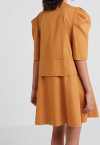 Sukienka z krótkim rękawem w musztardowym kolorze, z bufkami na ramionach, warstwowym krojem i rozkloszowanym dołem. Gładka faktura, casualowy fason.