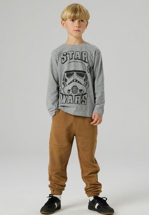 Grå langermet skjorte med Stormtrooper-grafikk og teksten «STAR WARS», kombinert med brune joggebukser. Svarte joggesko med hvite detaljer.