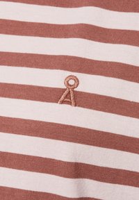 Nahaufnahme eines braun- und hellrosa gestreiften Stoffes mit einem kleinen, braun gestickten Logo, das einen Kreis über einem umgekehrten V zeigt.