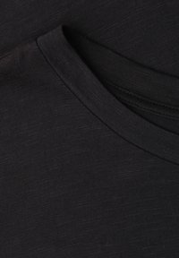 Gros plan d’un tissu noir montrant un col rond plié avec une texture côtelée visible et des détails de couture.