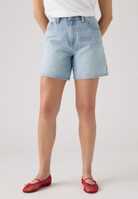 Lichtblauwe spijkershorts met een hoge taille, rechte snit en een nette zoom. Gecombineerd met rode mesh ballerina's.