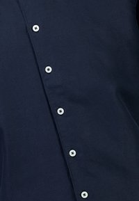 Marineblauwe button-up shirt van gladde stof, voorzien van witte knopen, een nette kraag en een eenvoudig ontwerp zonder patronen.