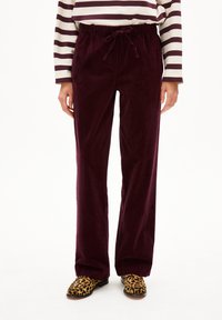 Bordeauxfarbene Cord-Hosen mit einem Kordelzugbund, ausgestattet mit einem geraden Bein Design. Kombiniert mit schwarzen und gelben Leo-Druckschuhen.