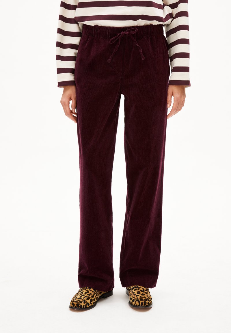 Bordeauxfarbene Cord-Hosen mit einem Kordelzugbund, ausgestattet mit einem geraden Bein Design. Kombiniert mit schwarzen und gelben Leo-Druckschuhen.