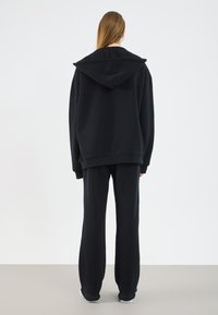 Svart oversized hettegenser med en stor hette, kombinert med matchende vide bukser. Laget av myk stoff, med en glatt overflate og avslappet passform.