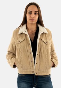 Chaqueta de pana beige con un cuello de borreguillo sintético blanco y dos bolsillos en el pecho. Los botones a presión y una tela texturizada crean detalles notables.