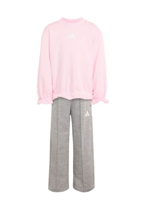 Rosa Sweatshirt mit langen Ärmeln und gerafften Bündchen, kombiniert mit weiten grauen Jogginghosen, beide mit weißem Adidas-Logo.