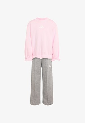 Roze trui met lange mouwen en gerimpelde manchetten, gecombineerd met grijze wijde joggingbroek, beide met wit Adidas-logo.
