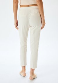 Cremefarvede slim-fit bukser med en glat tekstur, der har en mid-rise talje og to baglommer. Stylet med lyse flade sko.
