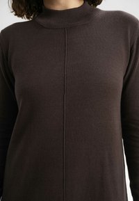 Dunkelbraunes Langarmoberteil mit hohem geripptem Kragen, das eine vertikale Naht an der Vorderseite und einen strukturierten Strickstoff aufweist.