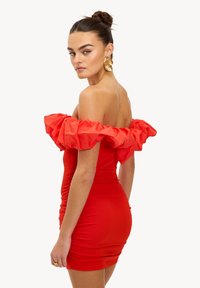 Robe rouge à épaules dénudées avec manches à volants, coupe ajustée, tissu extensible et texture froncée mettant en valeur la silhouette. Boucles d'oreilles dorées présentes.