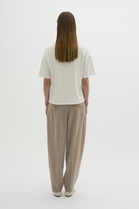 Vit topp med korta ärmar och avslappnad passform, kombinerad med beige randiga byxor. Outfiten har en mjuk textur och en enkel design.