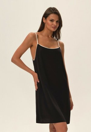 Czarna sukienka na ramiączkach z cienkimi paskami i białymi wykończeniami. Miękka tkanina, luźny krój, długość do połowy uda. Minimalistyczny design bez wzorów i ozdobnych elementów.