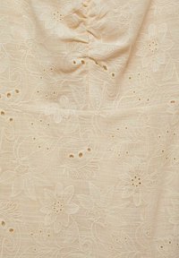 Tissu beige clair avec broderie florale et détails découpés. Texture lisse, design complexe avec feuilles et fleurs.