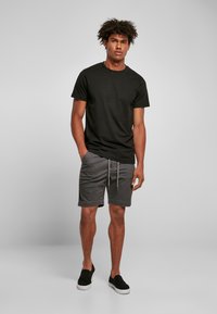 Tricou de bumbac negru, pantaloni scurți gri cu șnur, și pantofi slip-on negri. Stil casual, culori uni, fără modele sau grafică vizibile.