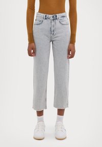 Jeans de tiro alto color azul claro, con pierna recta, dobladillos deshilachados y cinco bolsillos, combinados con una camiseta de manga larga mostaza y zapatillas blancas.