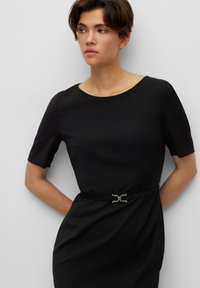 Black dress made from smooth fabric with short sleeves, a round neckline, and a decorative belt featuring a silver buckle at the waist.
