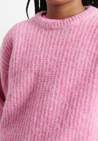 Pletený ružový sveter s vrúbkovanou textúrou a širokým okrúhlym výstrihom. Tkanina pôsobí jemne a útulne, s jemnými variáciami farieb.