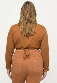 Brun bluse med lange ærmer og knyttet talje, parret med matchende brune bukser i rustfarve med baglommer og slim fit.