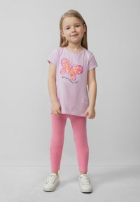 Roze t-shirt met korte mouwen, voorzien van een meerkleurig paillettenvlinderontwerp en de tekst "vind je blije vibes", gecombineerd met roze leggings.