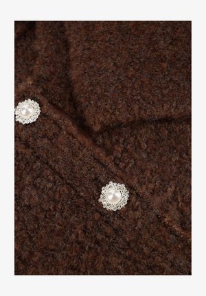 Bruine gestructureerde stof met duidelijke diepte; heeft twee decoratieve knopen met parelcentra omgeven door zilveren accenten.