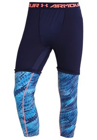 Shorts de compression bleu marine avec des leggings bleus à motif attachés, présentant des coutures latérales corail et une ceinture corail avec le logo Under Armour.