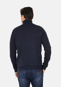 Maglione lavorato a maglia blu navy con colletto alto, polsi e orlo a costine. Indossato con jeans di denim blu dotati di tasche posteriori.