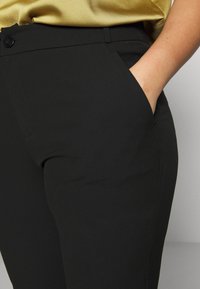 Svarta skräddarsydda byxor i mjukt tyg, med en smal passform och sidofickor. Midjebandet har en knappstängning för extra detaljer.