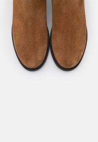 Stivaletti alla caviglia in camoscio marrone con una texture liscia, punta arrotondata e suola in gomma nera a contrasto, visti dall'alto.