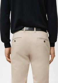 Pantaloni beige con una texture liscia, due tasche posteriori e dettagli con bottoni neri, abbinati a un maglione nero aderente.