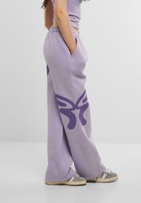 Lösa lavendelfärgade sweatpants i bomull, med sidofickor och en stor lila fjärilsuppgift på vänster ben.