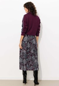 Sweatshirt bordeaux avec des rayures blanches sur les manches, associé à une longue jupe à motifs floraux noir et blanc et des bottes noires jusqu'aux genoux.