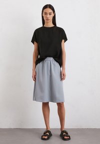 Haut noir à manches courtes, jupe taille élastique gris clair, et sandales noires. Tissu lisse, coupe décontractée, jupe longueur genou avec de subtils plis.