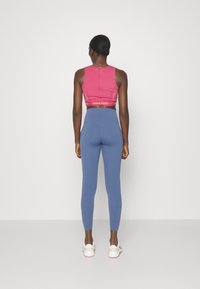 Różowy biustonosz sportowy z żółtymi akcentami, niebieskie legginsy z wysokim stanem, gładka tkanina, dopasowany fason, widok od tyłu, minimalistyczne tło.