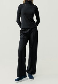 Black long-sleeve turtleneck top paired with loose black trousers and blue athletic sneakers. Smooth fabric with minimal detailing.