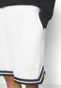 Witte mesh sportshorts met een zwarte tailleband, voorzien van zwarte zijstrepen en een neon groene "ULTRA" logo op de onderste zoom.