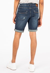 Denim shorts in een donkere wash met opgerolde zomen, met een verouderde textuur, twee achterzakken en een bruine leren patch op de tailleband.