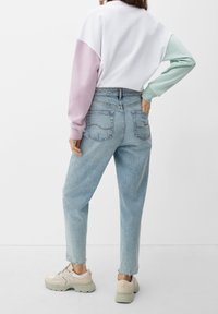 Mikina s bloky šedé a růžové barvy s dlouhými rukávy, doplněná světle modrými džínami s kapsami a mírným opráním.