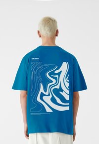 Turkis bomuld t-shirt med et hvidt abstrakt design på ryggen, korte ærmer og afslappet pasform. Tekst på den øverste ryg.