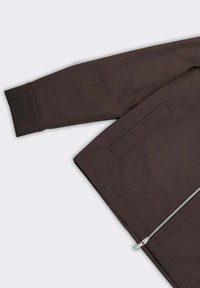 Giacca marrone strutturata con chiusura a zip, tasca laterale e polsino a costine. Tessuto liscio e strutturato con linee pulite e design sartoriale.
