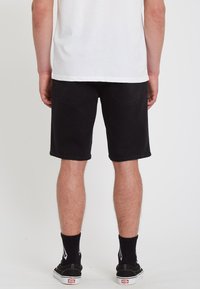 Shorts en denim noir avec une coupe droite et des coutures visibles. Portés avec une chemise blanche, des chaussettes noires et des baskets noires.
