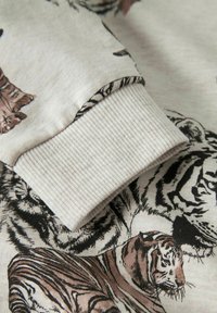 Kokvilnas džemperis ar bēša krāsas fonu, uz kura ir dažādi brūnas un melnas krāsas tīģera raksti. Piedurkņu gali ir adīti riboti un teksturēti.