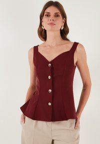 Bordo bezrukavni top s V-izrezom, sa tijesnim korzetom, pet dekorativnih srebrnih dugmadi sprijeda i raširenim peplum donjim dijelom.