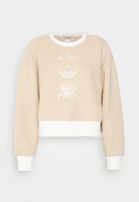 Beige kortärmad sweatshirt gjord av mjuk fleece, med vita broderade motiv, ribbade detaljer och en kontrasterande vit band vid nederkanten och ärmsluten.
