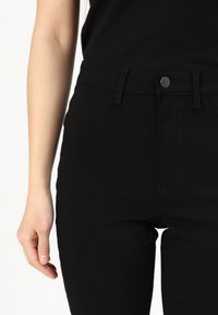 Svarta åtsittande jeans med en slät textur, med framfickor, knappstängning och kontrasterande sömmar längs sömmarna.