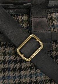 Cintura in pelle nera con una fibbia in metallo dorato, attaccata a un tessuto testurizzato con un motivo houndstooth verde, blu e marrone.