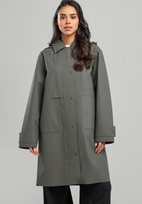 Khaki vesimproof takki, jossa on napitus edessä, suuret taskut ja leveät hihansuut. Takki on valmistettu sileästä, rakenteellisesta materiaalista ja siinä on kaulus.